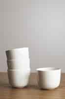 Foto gratuita vista lateral de forma recta en blanco blanco simple tazas de café en pirámide sobre mesa de madera gruesa aislada