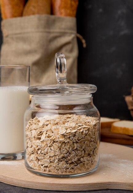 Vista lateral del frasco de vidrio con copos de avena y leche sobre superficie de madera y fondo negro con espacio de copia