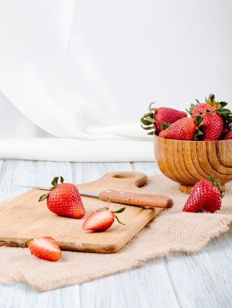 Vista lateral fresa fresca en un tazón cuchillo y placa sobre fondo blanco.