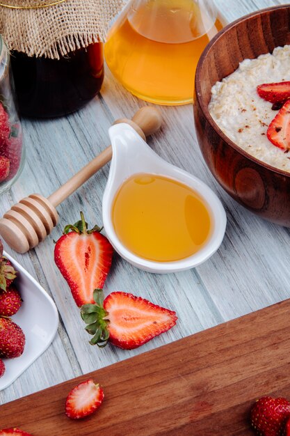 Vista lateral de fresas frescas maduras en un tablero de madera con gachas de miel y avena en un tazón de madera en rústico_