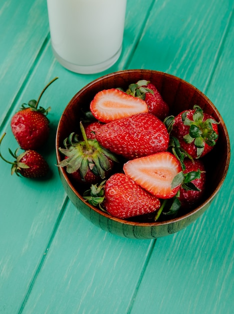 Foto gratuita vista lateral de fresas maduras frescas en un tazón de madera con un vaso de leche en madera verde