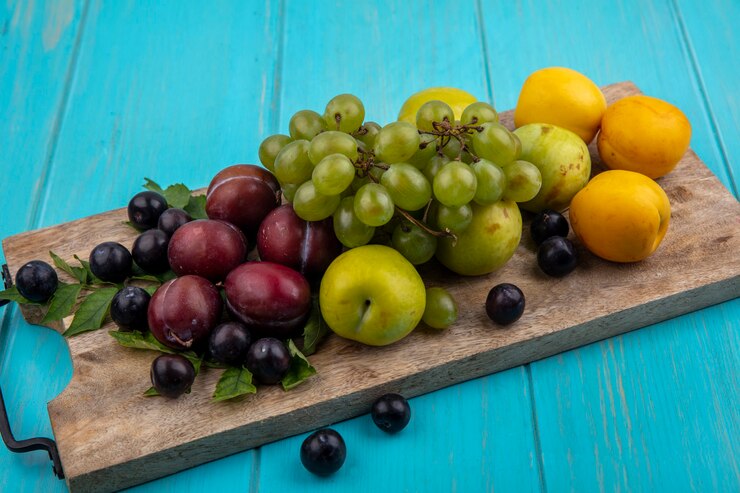 Foto gratuito vista lateral de frutas como nectacots pluots de uva con hojas sobre tabla de cortar y uvas sobre fondo azul