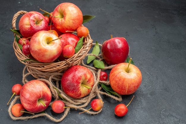 Vista lateral frutas manzanas cerezas en la canasta junto a las frutas y cuerda