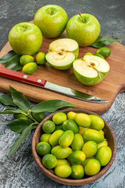 Vista lateral de frutas manzanas verdes y cuchillo en el tazón de fuente de la tabla de cortar de frutas cítricas