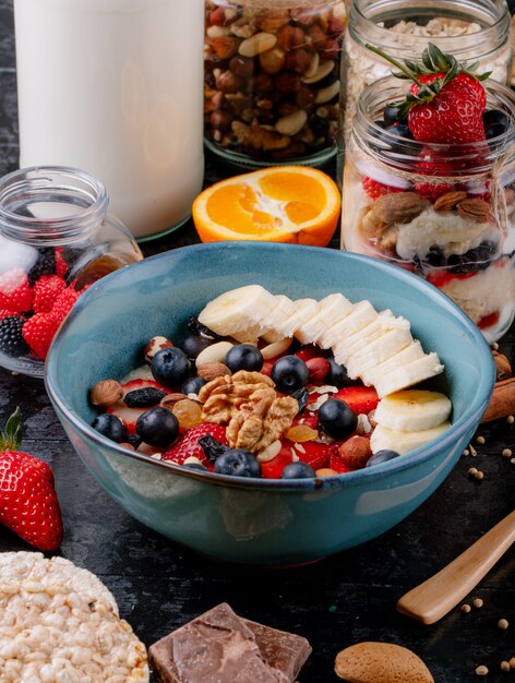 Vista lateral de gachas de avena con fresas, arándanos, plátanos, frutas secas y nueces en un tazón de cerámica sobre la mesa