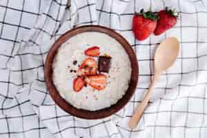 Foto gratuita vista lateral de gachas de avena con fresas frescas maduras y chocolate en un tazón de madera y una cuchara sobre tela escocesa