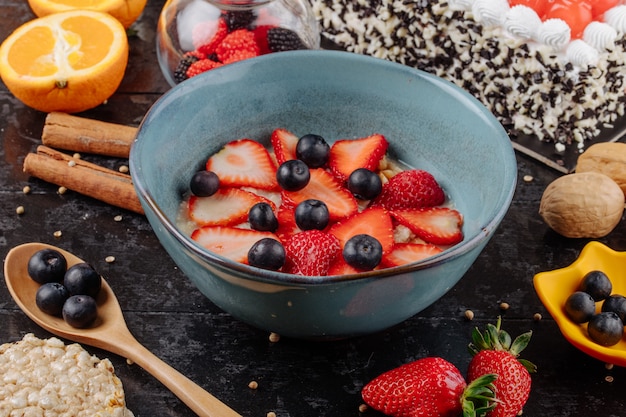 Vista lateral de gachas de avena con rodajas de fresas y arándanos en un tazón de cerámica sobre la mesa