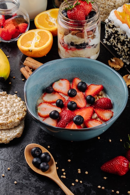 Foto gratuita vista lateral de gachas de avena con rodajas de fresas y arándanos en un tazón de cerámica sobre la mesa