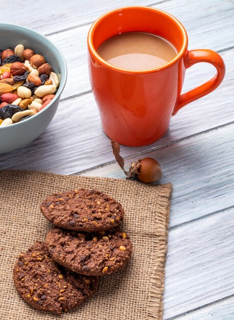 Vista lateral de galletas de avena con chispas de chocolate y nueces con una taza de bebida de cacao en una madera