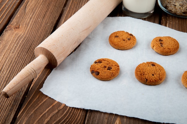 Foto gratuita vista lateral de galletas de avena en papel de calco y un rodillo sobre un fondo de madera