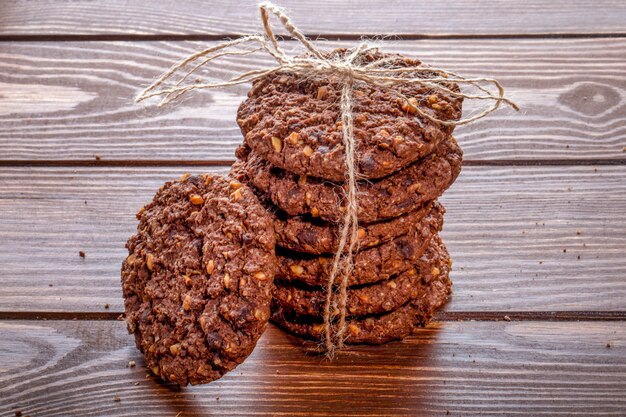 Vista lateral de las galletas de chispas de chocolate con cereales, nueces y cacao atados con una cuerda sobre fondo de madera