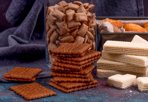 Vista lateral de galletas de chocolate y crujientes waffles sobre fondo oscuro