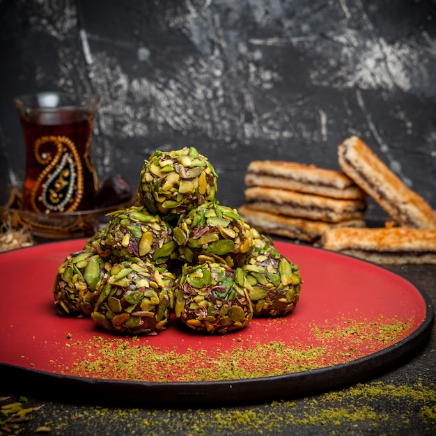 Foto gratuita vista lateral galletas de pistacho en la plataforma redonda roja con galletas y té sobre fondo oscuro con textura.