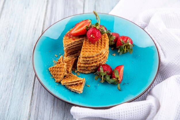 Vista lateral de galletas waffle y fresas en placa sobre madera