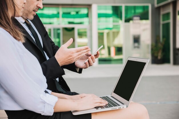 Vista lateral de gente de negocios sentados en banco con portátil