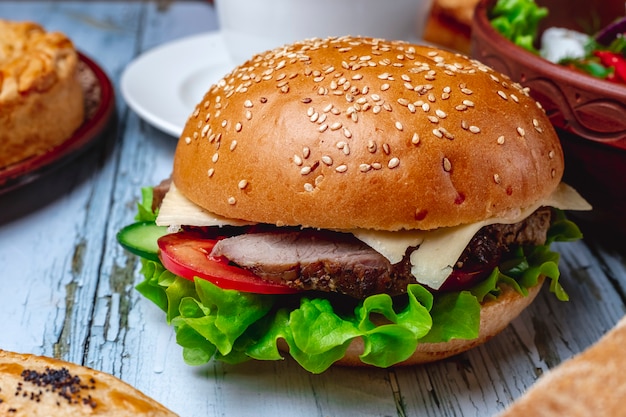 Vista lateral hamburguesa con carne a la parrilla, queso, lechuga y tomate entre bollos de hamburguesa