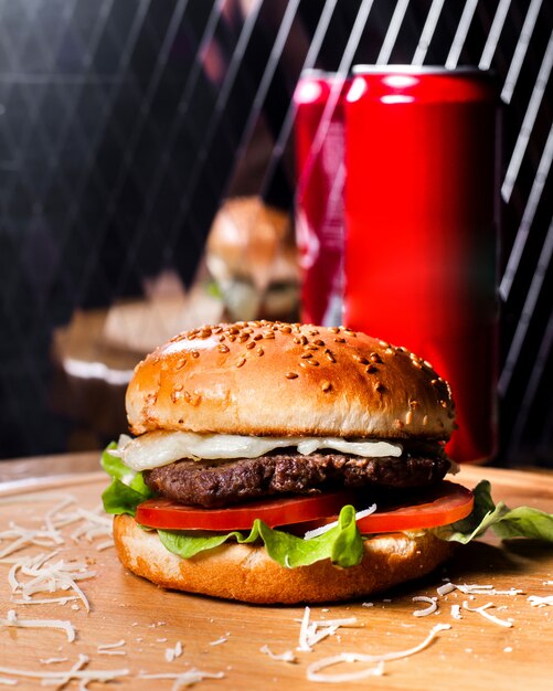 Vista lateral de la hamburguesa con carne de res queso derretido y verduras sobre tabla de madera