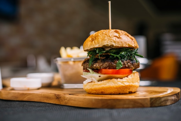 Vista lateral de hamburguesa con chuleta de ternera hierbas y tomate sobre una plancha de madera