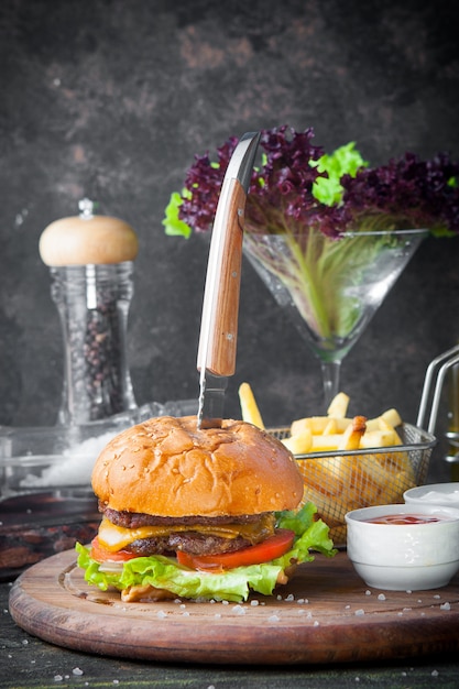 Vista lateral hamburguesa con cuchillo y tazón para salsa y papas fritas en bandeja de comida de madera en el restaurante