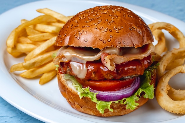 Vista lateral hamburguesa con empanada de carne a la parrilla tocino frito lechuga con queso cebolla roja tomate y papas fritas en un plato