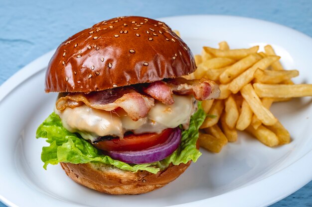 Vista lateral hamburguesa hamburguesa de ternera a la parrilla tocino frito lechuga tomate cebolla roja y papas fritas en un plato