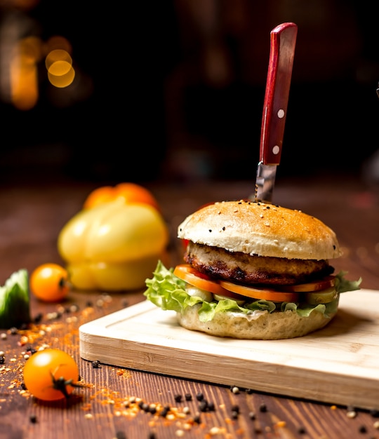 Vista lateral hamburguesa de pollo con hojas de lechuga empanada de pollo con tomate en bollos de hamburguesa y pimienta negra sobre la mesa