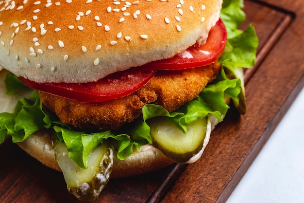 Vista lateral hamburguesa de pollo con rodajas de tomate y lechuga en el tablero