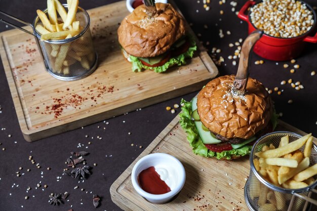 Vista lateral hamburguesas con papas fritas ketchup y mayonesa en soportes con cuchillos