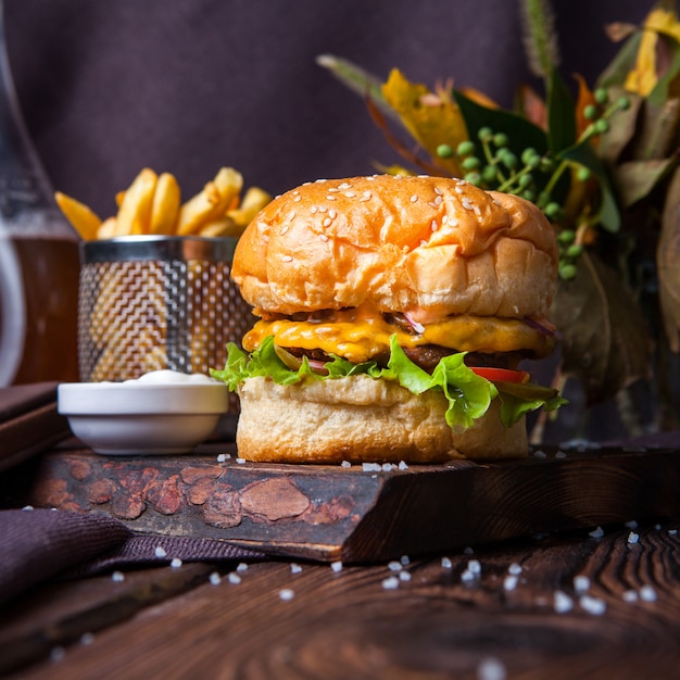 Vista lateral de hamburguesas y papas fritas sobre un fondo negro y madera con decoraciones