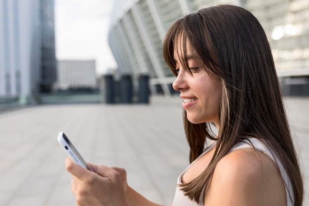 Vista lateral hermosa joven sonriente mientras mira su teléfono