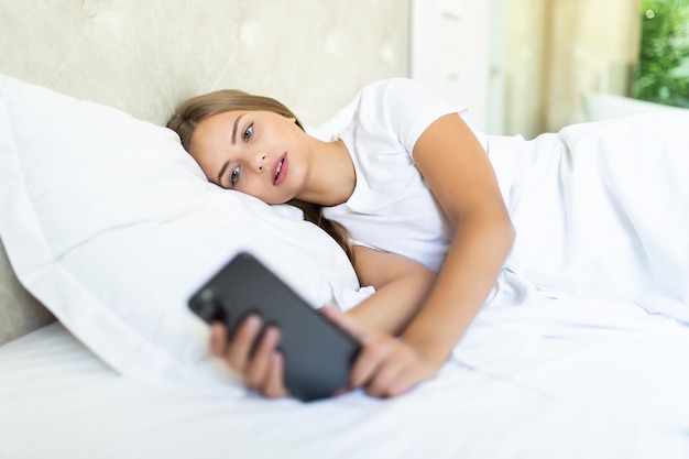 Vista lateral de la hermosa mujer mirando un teléfono móvil mientras está acostado en la cama