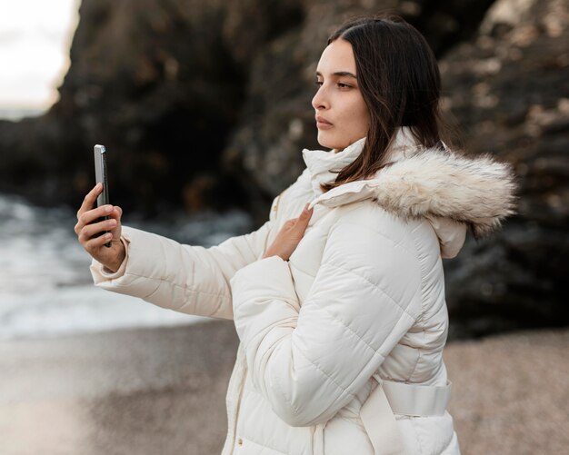 Vista lateral de la hermosa mujer en la playa tomando fotografías con el teléfono inteligente