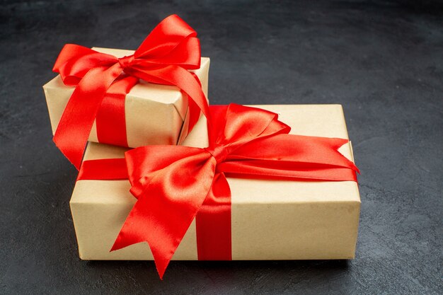 Vista lateral de hermosos regalos con cinta roja sobre fondo oscuro