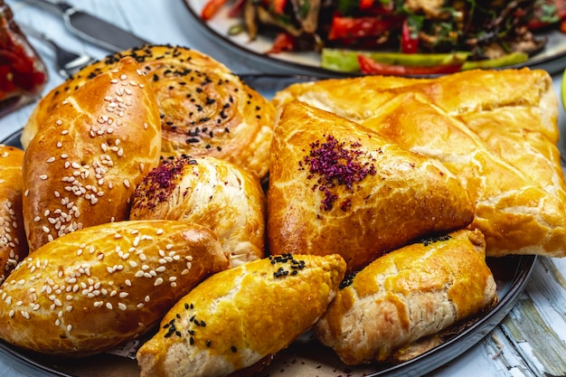 Vista lateral hojaldres con semillas de sésamo de carne molida y tortas rellenas con puré de papa sobre la mesa