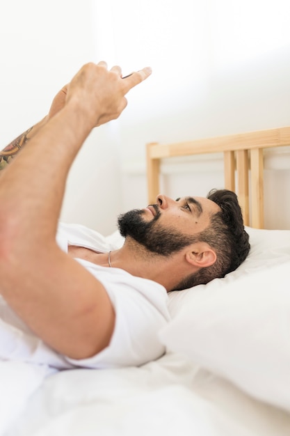 Foto gratuita vista lateral de un hombre acostado en la cama con teléfono móvil