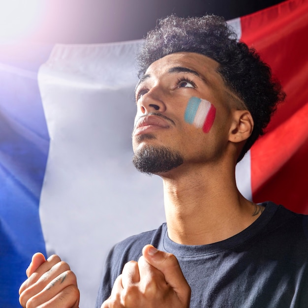 Vista lateral del hombre con bandera francesa mirando hacia arriba y sosteniendo los puños juntos