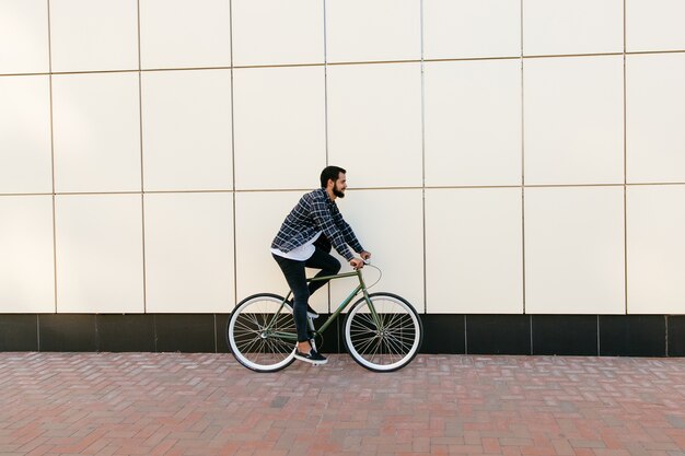 Vista lateral de un hombre barbudo elegante que monta una bicicleta en la calle de la ciudad.