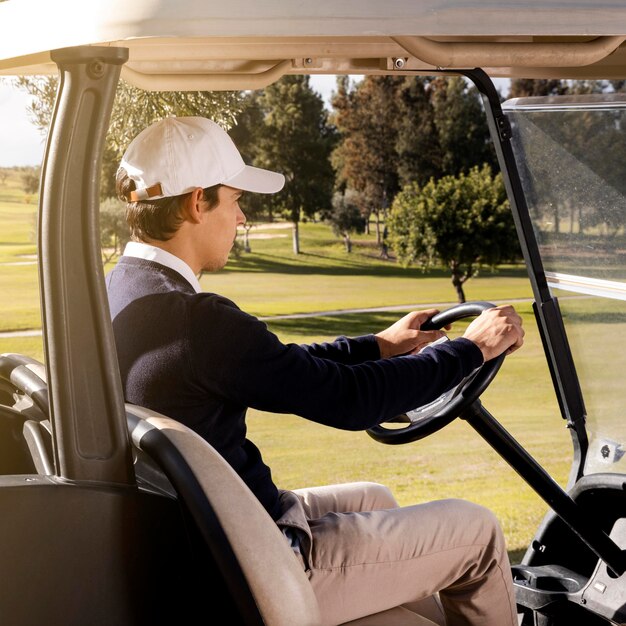 Vista lateral del hombre conduciendo un carrito de golf en el campo