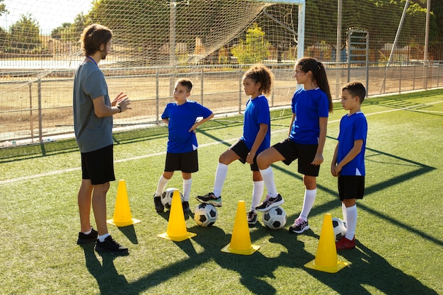 Vista lateral hombre entrenando niños jugando al fútbol