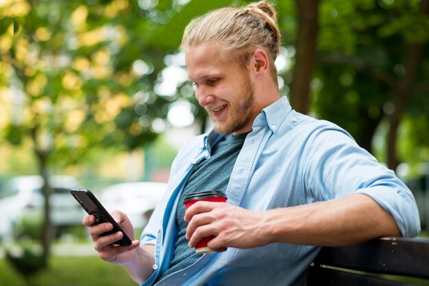 Vista lateral del hombre feliz al aire libre con teléfono inteligente y taza