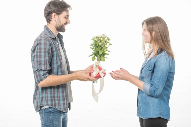 Foto gratuita vista lateral de un hombre feliz que da el regalo y la flor a su novia en el fondo blanco