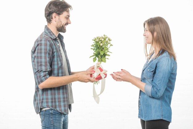 Vista lateral de un hombre feliz que da el regalo y la flor a su novia en el fondo blanco