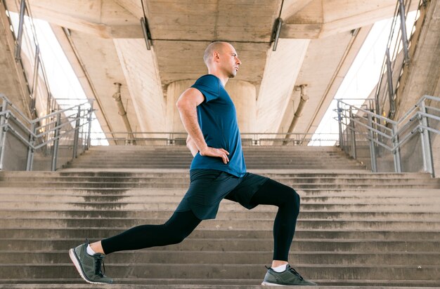 Vista lateral de un hombre de fitness haciendo ejercicios de estiramiento de pie en la escalera