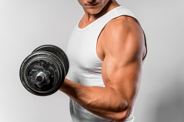 Vista lateral del hombre en forma con camiseta sin mangas mostrando bíceps mientras sostiene peso