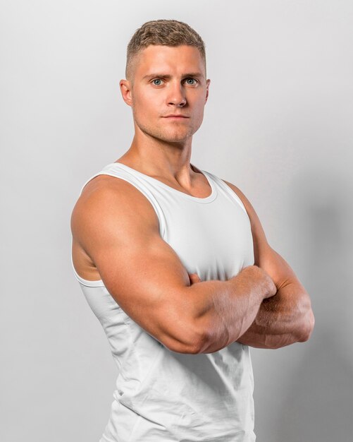 Vista lateral del hombre en forma posando mientras usa camiseta sin mangas con los brazos cruzados