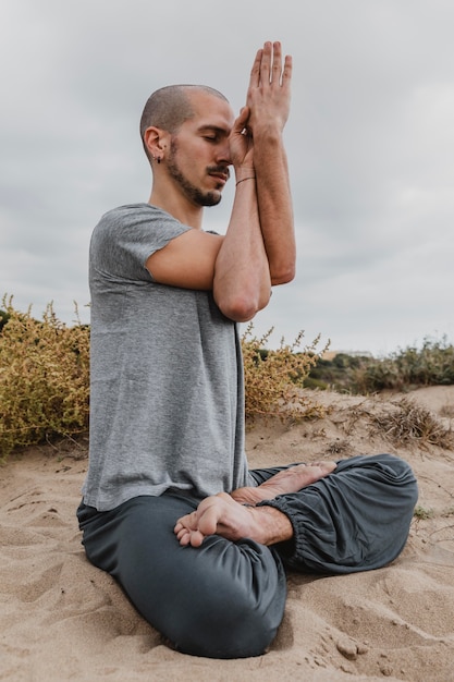 Vista lateral del hombre fuera meditando mientras hace yoga