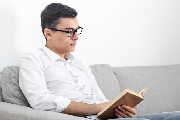 Foto gratuita vista lateral del hombre con gafas y libro de lectura en el sofá