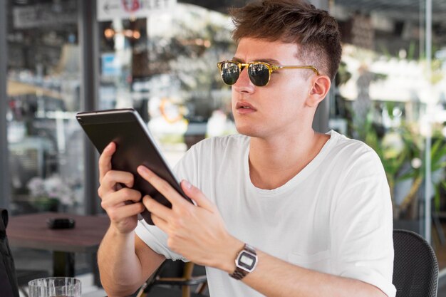 Vista lateral del hombre con gafas de sol mirando tableta mientras está en el pub