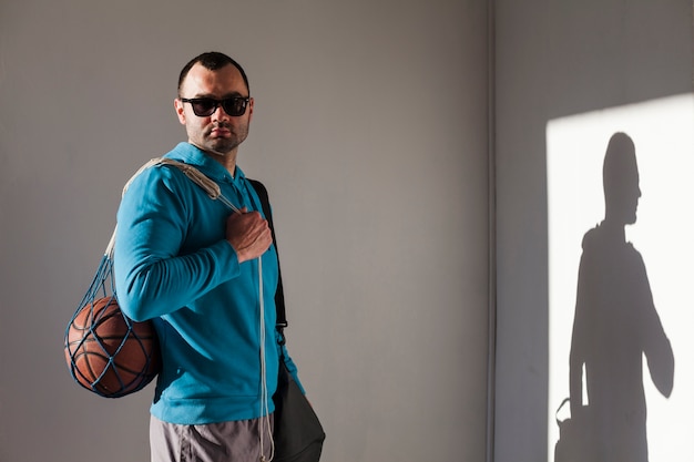 Foto gratuita vista lateral del hombre en gafas de sol y sudadera con capucha con baloncesto en red