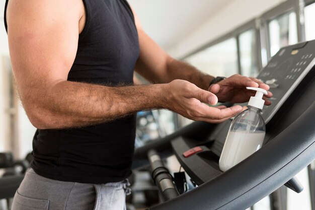 Vista lateral del hombre en el gimnasio con desinfectante de manos